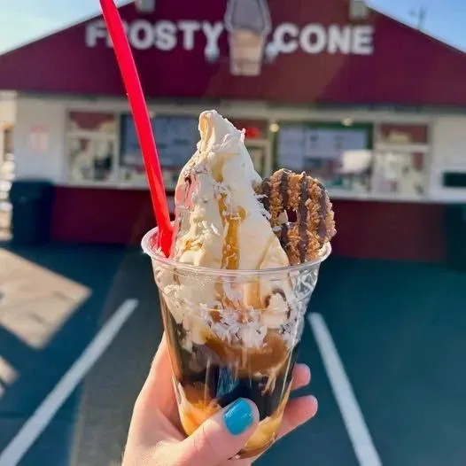 Sundae in a cup with a red straw, held up in front of the Frosty Cone stand