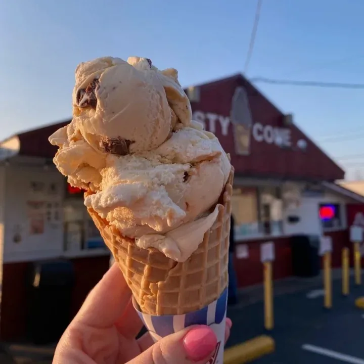 Ice cream in a waffle cone held up in front of the Frosty Cone stand