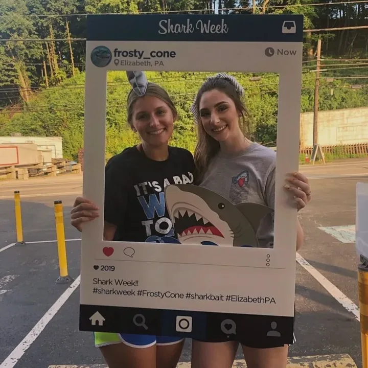 Two people holding a Shark Week photo frame in the parking lot