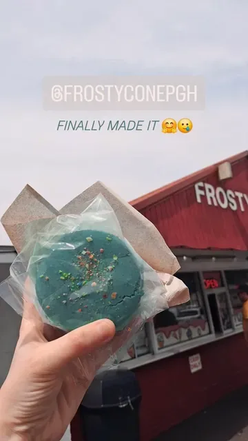 Blue ice cream cookie sandwich in a wrapper, held up in front of the stand