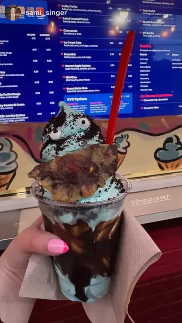 Blue Cookie Monster parfait with candy eyes and a cookie, held up at the menu board