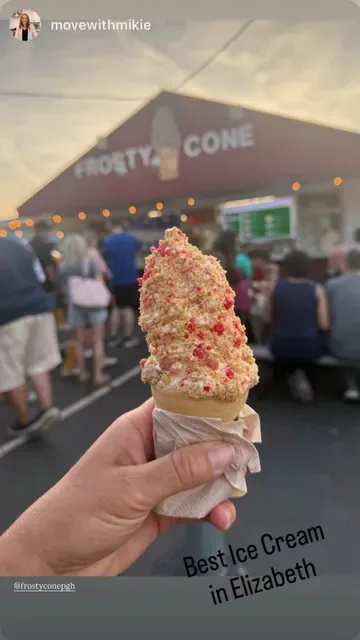 Cone covered in red and golden crunch topping in front of the stand at sunset