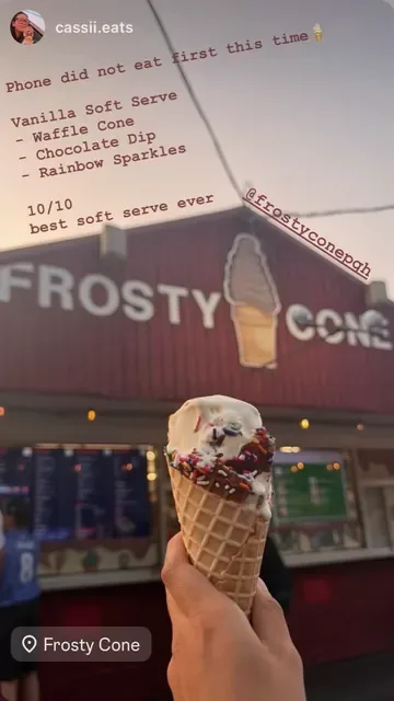 Vanilla soft serve in a waffle cone with chocolate dip and rainbow sprinkles in front of the stand